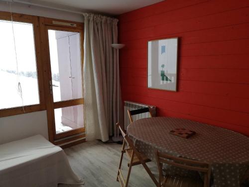 Cette chambre rouge comprend une table, un lit et une fenêtre. dans l'établissement Appartement cosy à Plagne Village avec accès direct aux pistes, terrasse exposée sud, animaux acceptés - FR-1-351-22, à La Plagne
