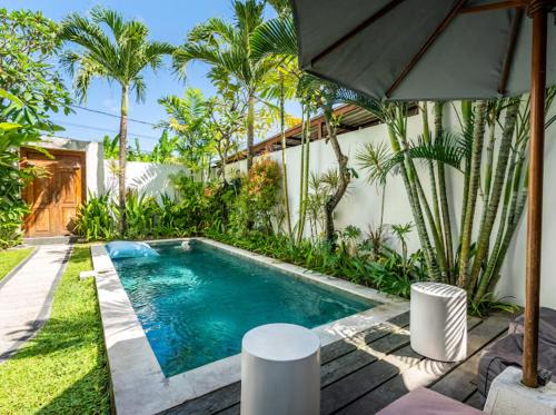 a swimming pool next to a house with palm trees at Kubu Guest House in Seminyak