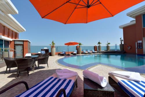 a swimming pool with chairs and an umbrella at Ramada by Wyndham Manama City Centre in Manama