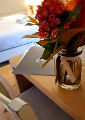 a vase with red flowers on a table next to a book at Agriturismo B&B Casa Bortolin in Valdobbiadene