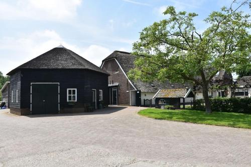 a black barn with a tree and a driveway at Chalet 4, Recreatie aan de Vecht in Weesp