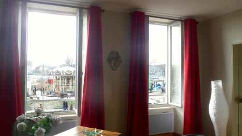 Cette chambre dispose de deux fenêtres avec des rideaux rouges. dans l'établissement L'Appart Du Vieux Port, à La Rochelle