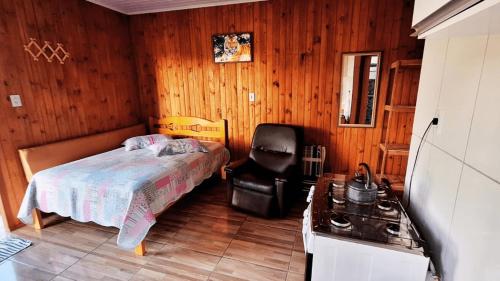 a bedroom with a bed and a chair and a stove at Chalézinho Bons Ventos Campestre no Sitio com Churrasqueira WI-FI a 6km da Estrada do Mar 7km Parque de Rodeio II 8,1Km Prefeitura II 7,2Km UFRGS Litoral II Taxi Fácil II Tranquilidade 12km Praias Tramandai in Osório
