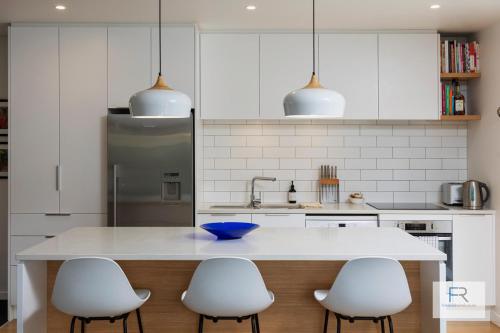 a kitchen with a white counter and four white chairs at Stylish Northcote Point Bungalow in Auckland