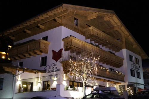 a large white building with wooden balconies and a tree at Appartements Der Fuchsbau in Saalbach Hinterglemm