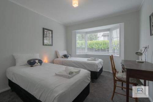 オークランドにあるCosy Bayswater Houseのベッド2台と机と窓のある部屋