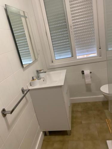 a white bathroom with a sink and two windows at Despierta frente al mar en Moaña in Pontevedra