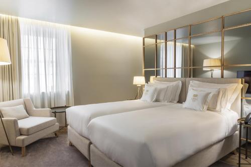 a bedroom with a large white bed and a chair at Casa da Companhia Hotel & Spa, Vignette Collection by IHG in Porto