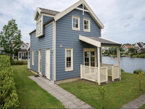 a blue house with a porch and a body of water at Bungalow in South Holland with Private Jetty in Simonshaven