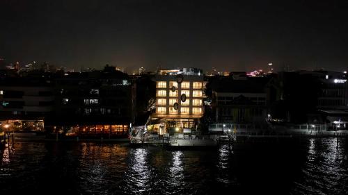a lit up building on the water at night at The StandardX, Bangkok Phra Arthit in Bangkok