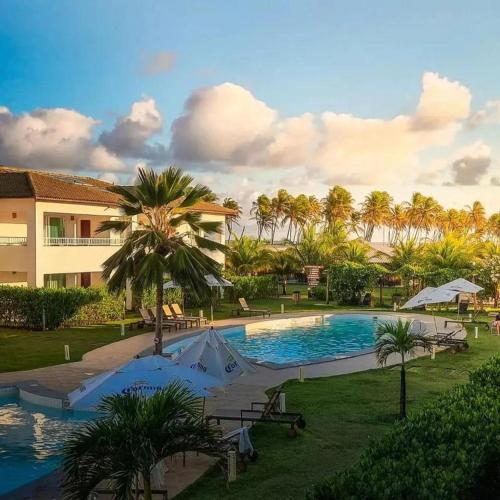 a resort swimming pool with palm trees and a building at Apartamento 03 suítes - Tree Bies Beach Resort - Praia de Subaúma in Entre Rios