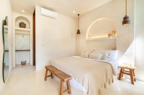 Dormitorio blanco con cama y banco de madera en Casa Admire Villas, en Legian