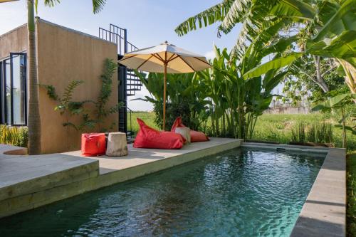 - une piscine avec des oreillers rouges et un parasol à côté d'une maison dans l'établissement Wander Havens, à Canggu