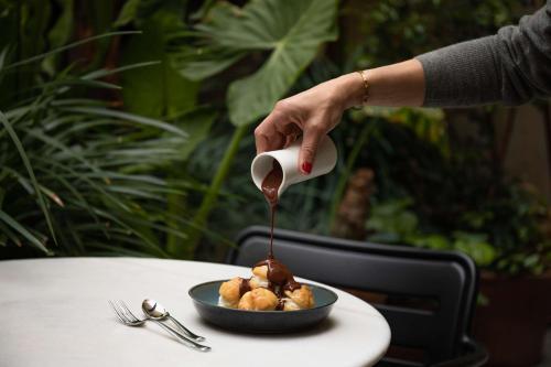 a person pouring sauce into a bowl of food at Alexandra Barcelona Hotel, Curio Collection by Hilton in Barcelona