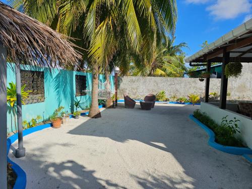 a patio with palm trees and a blue building at Garden Rooms by Lagoon View in Bodufolhudhoo