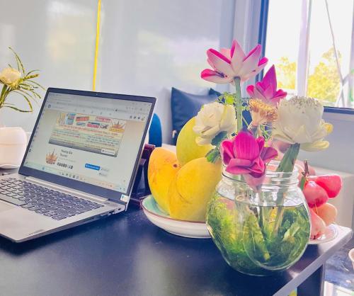 a laptop computer sitting on a table with flowers in a vase at HOMESTAY Hoàng GIa in Ấp Ông Tú