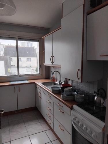 une cuisine avec des armoires blanches, un évier et une fenêtre dans l'établissement Douric, à Brest