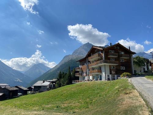 a building on a hill with mountains in the background at Hotel Etoile & Alpenperle Residences in Saas-Fee