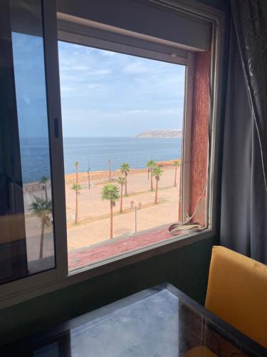 a window with a view of the ocean and palm trees at Vu sur corniche in Safi