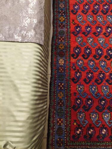 a red and blue rug next to a bed with a pillow at Guest House Ruh Achari in Sheki