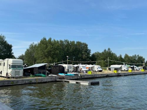 a group of vehicles parked next to a river at Houseboot Cormorant, lake view in Biddinghuizen
