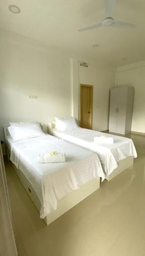 two beds in a room with white sheets and towels at Thooru stay in Kelaa