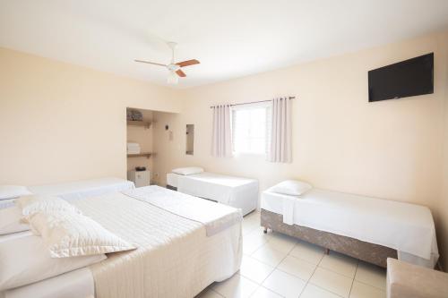 a white bedroom with two beds and a flat screen tv at Pousada Mirante das Estancias in Águas de Lindóia