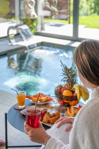 a woman sitting at a table next to a swimming pool at Chalet Soleil Bœuf et Spa de l'adouss in Saint-Jean-Saint-Nicolas