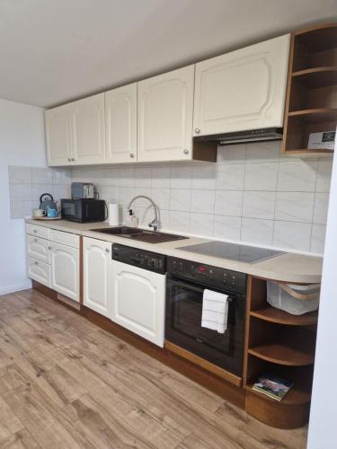 a kitchen with white cabinets and a black dishwasher at Baráti Vendégház in Győrújbarát