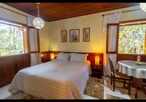 a bedroom with a bed and a table and a window at Chalés Caminho das Montanhas in Monte Verde