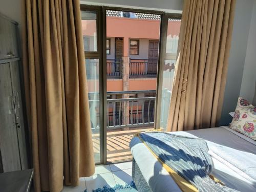 a bedroom with a bed and a window with a balcony at A47 self catering apartment inside Bains Lodge in Bloemfontein