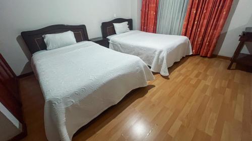 two beds with white sheets in a room with wooden floors at Internacional El Nogal Ipiales in Ipiales