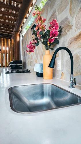 a kitchen sink with a vase of flowers on a counter at Casa Turquesa Pé na areia Piscina infinita Pet friendly Condomínio fechado in Itacimirim