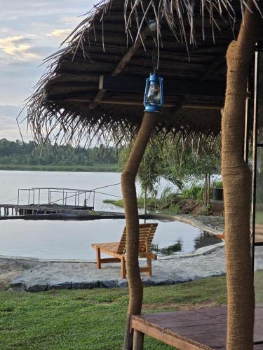 a straw hut with a bench next to a lake at Nagara Lake Glamping Resort in Hambantota