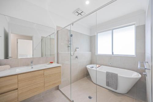 a white bathroom with a tub and a sink at The Waybre - walk to the beach, ducted aircon in Dunbogan