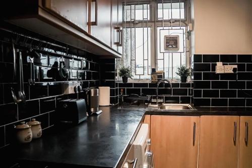 una cocina con paredes de azulejos negros y fregadero en Spacious 3 Bedroom Flat, en Londres