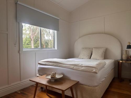 a white bedroom with a bed and a table at Kookaburra Retreat in Daylesford