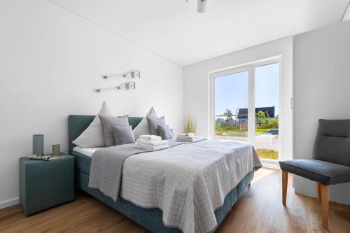 a white bedroom with a bed and a chair at Maltes-Ostseekoje Parken frei vorm Haus, 500m zum Strand,Infrarotsauna,Magenta TV mit Netflix ,Disney TVund Rtl plus, Kaminofen im Wohnzimmer,ab Oktober Brennholz gratis Fahrradschuppen,Mückenschutz in Olpenitz
