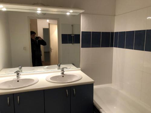 un homme prenant une photo d'une salle de bains avec deux lavabos et une baignoire dans l'établissement Appartement T3, à Bagnères-de-Bigorre
