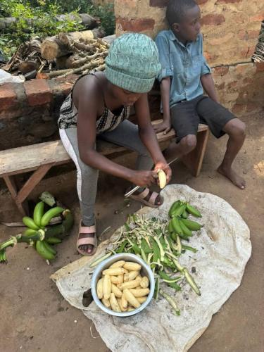 a woman cutting up bananas and a bowl of vegetables at Kibale Cultural Homestay in Fort Portal