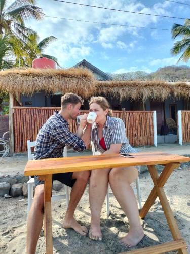 a man and woman sitting at a picnic table on the beach at Sentigi Homestay Gili Gede in Gili Gede