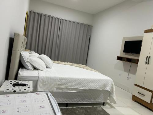 a white bedroom with a bed and a television at Madeira Lofts - Centro Juina in Juína