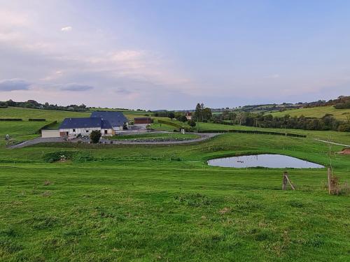 a large green field with a house and a pond at Gîte la Belle des Champs in Saint-Saire