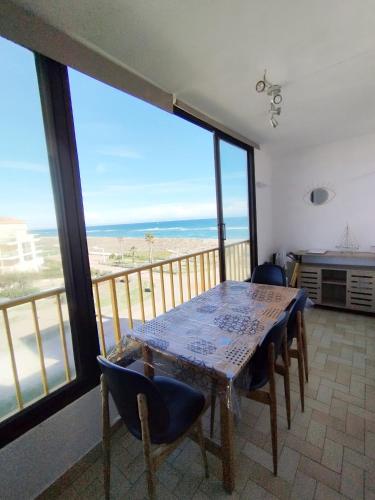une table et des chaises dans une pièce avec une grande fenêtre dans l'établissement Appartement vue mer Le Barcarès, au Barcarès