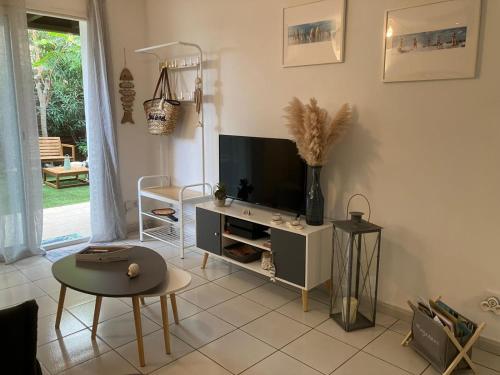 un salon avec une télévision et une table dans l'établissement Appartement 4 étoiles avec jardin clôturé et piscine dans la résidence - Narbonne Plage, à Narbonne