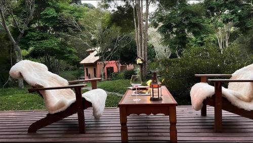 a wooden deck with two chairs and a table with wine glasses at CHALÉ AZALÉA Lindo chalé NO CAMPO com roupas de cama e banho impecáveis, Wi-Fi StarLink de alta velocidade, cozinha equipada, estacionamento privativo, decks, jardins, lareiras, conforto, privacidade e belíssimas paisagens in Cunha
