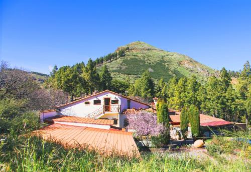 una mujer parada frente a una casa con una montaña en Hotel Rural El Refugio - Adults Only, en Tejeda