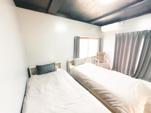 two beds in a room with a chair and a window at まるとくハウス和歌山 in Wakayama