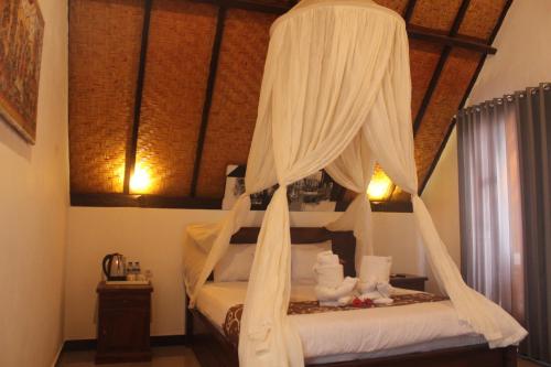 a bedroom with a canopy bed with white drapes at Maskot Penida Cottage in Nusa Penida