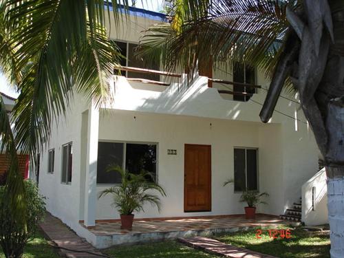 a white house with palm trees in front of it at BONITO APARTAMENTO RODEADO DE PALMERAS primer nivel in Barra de Navidad
